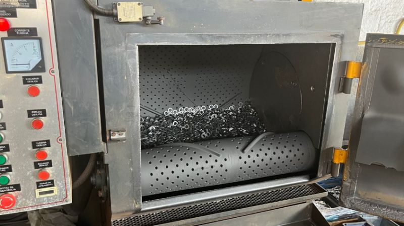 Peças metálicas dentro de máquina de jateamento abrasivo rotativo